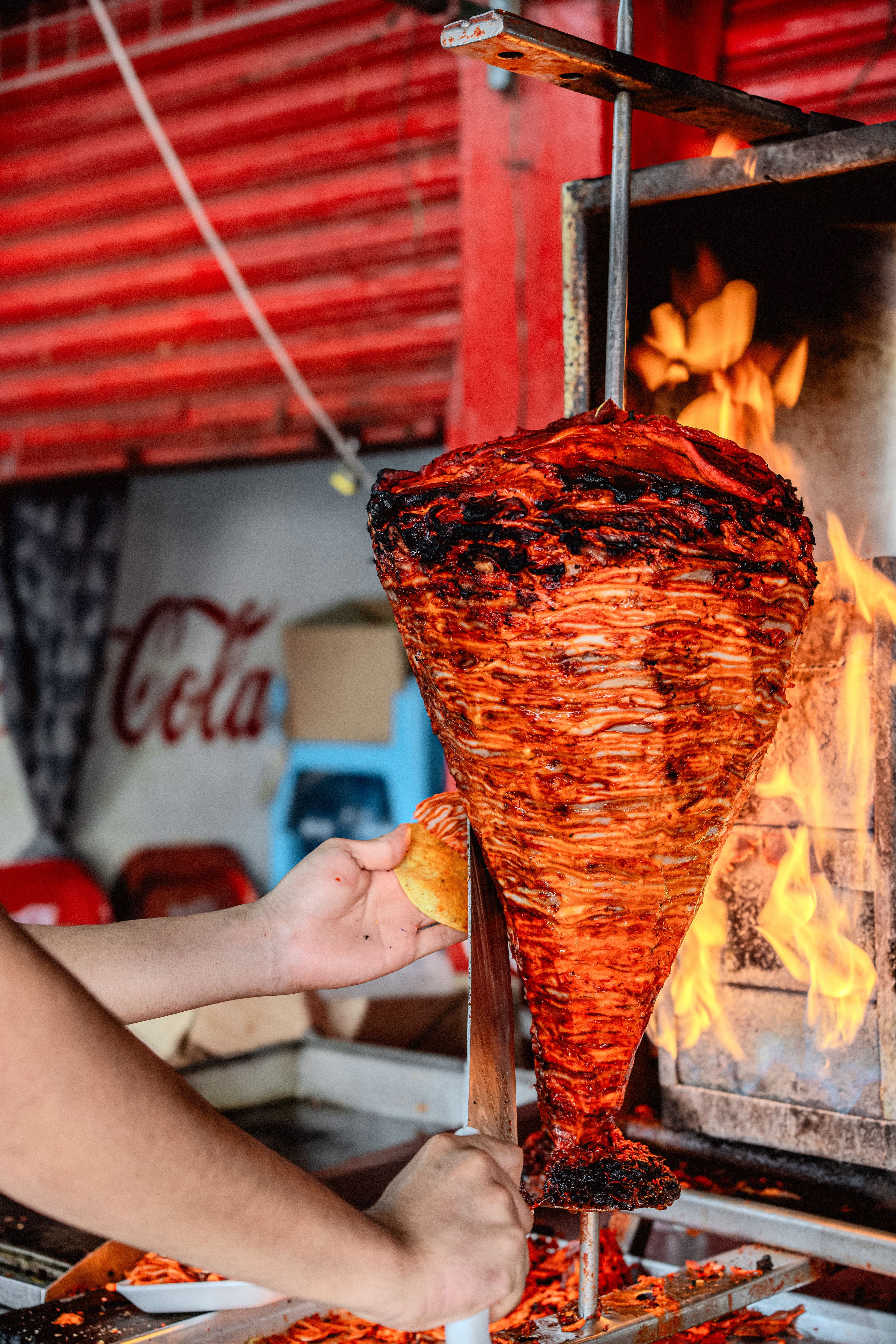 An al pastor trompo crowned with a pineapple beside the flame
