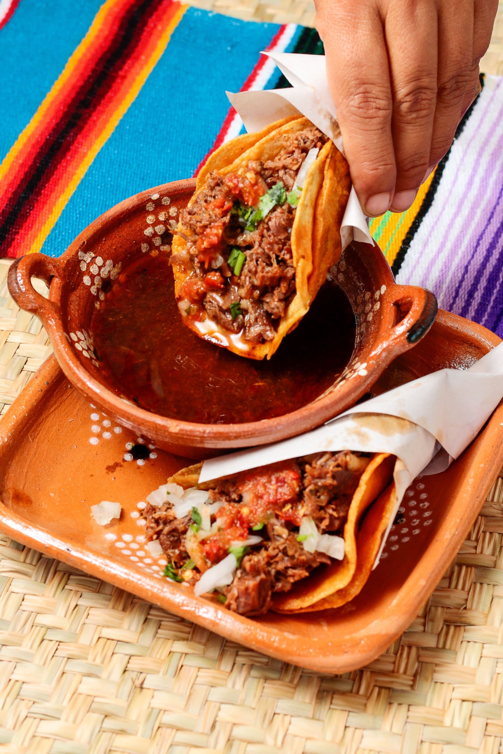 Birria tacos beside a cup of red consome